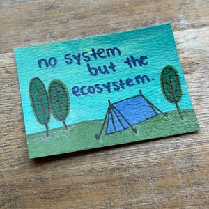 May include: A hand-painted card with the text "no system but the ecosystem." The card features a blue tent, green trees, and a green field against a teal sky. The artwork is on a textured paper surface.