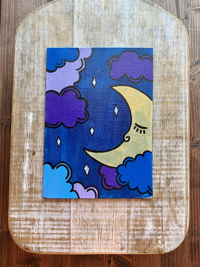 May include: A hand-painted canvas with a crescent moon and clouds in shades of purple, blue, and yellow against a dark blue background. The moon has a closed eye and a small smile.
