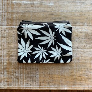May include: A small black zippered pouch with a white marijuana leaf pattern.