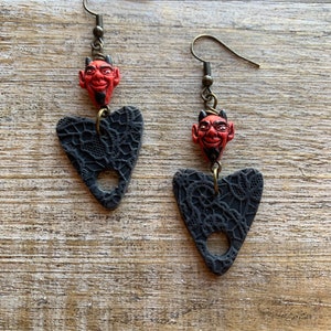 May include: A pair of black heart-shaped earrings with a lace design and a red devil head charm hanging from each earring.