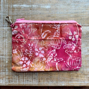 Op de afbeelding: Een roze ritszakje met een bloemenprint in tinten roze, oranje en wit. Het zakje heeft een zilveren rits.