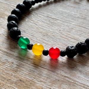 May include: A black lava rock bracelet with green, yellow, and red beads. The bracelet has a silver clasp.
