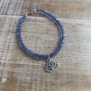 May include: A blue beaded bracelet with a silver lotus charm. The bracelet is made of small, square beads and has a simple clasp.