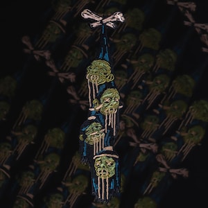 Könnte beinhalten: Gestickter Aufnäher mit einem vertikalen Design aus grünen Zombie-Köpfen mit tropfenden Details, vor einem dunkelblauen und schwarzen Hintergrund. Der Aufnäher ist mit einem Knochenmuster versehen. Der Hintergrund hat ein sich wiederholendes Muster aus Totenköpfen und gekreuzten Knochen.