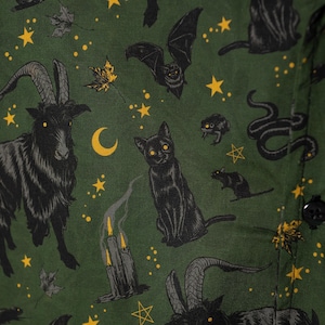 Puede incluir: Tela verde oscuro con un patr&oacute;n repetido de cabras, gatos, murci&eacute;lagos, serpientes, ratas, conejos, estrellas, lunas y velas negras. El dise&ntilde;o tiene un tema espeluznante de Halloween.