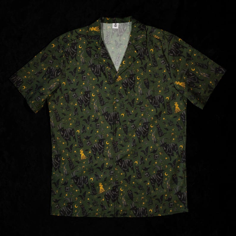 Puede incluir: Camisa verde con botones con un estampado repetido de gatos negros, murci&eacute;lagos, lunas, estrellas y figuras de brujas. La camisa de manga corta tiene cuello en V y est&aacute; hecha de tela ligera.