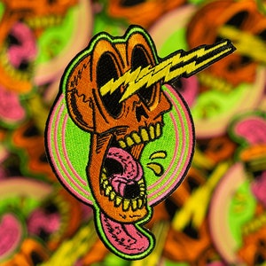 May include: A bright orange embroidered patch of a cartoon skull with lightning bolts shooting out of its eyes. The skull is wearing a pink tongue that is sticking out and dripping with yellow saliva. The skull is surrounded by a green and pink circle.