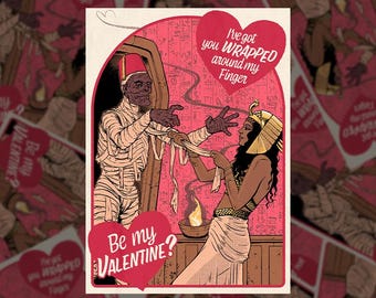 Può includere: Illustrazione di biglietto di San Valentino con una mummia e una regina egizia. La mummia, avvolta in bende, si protende verso la regina, che tiene le bende. Il testo del biglietto include "Be my Valentine?" e "I've got you wrapped around my finger."