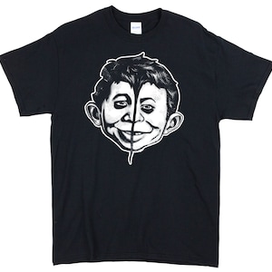 May include: Black t-shirt with a white graphic of a split-faced character with a mohawk.
