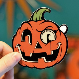 May include: A cartoon pumpkin with a mischievous grin, wearing an eye patch and a single tooth. The pumpkin is orange with black eyes and a black mouth.