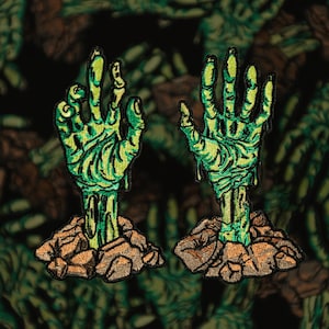Op de afbeelding: Twee geborduurde patches met groene zombiehanden die uit de grond komen. De handen zijn gedetailleerd met aderen en druipend groen spul, tegen een bruine en zwarte achtergrond. De patches zijn ontworpen voor kleding.