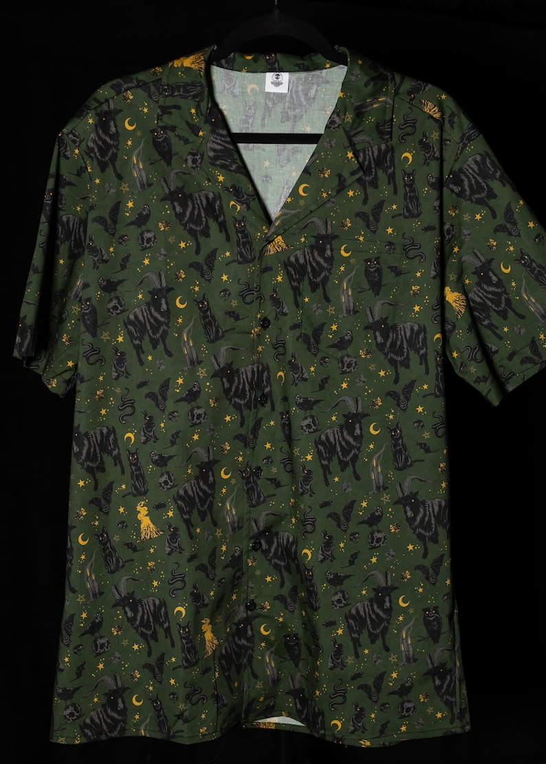 Puede incluir: Camisa verde con botones con un estampado repetido de cabras negras, gatos, murci&eacute;lagos, lunas, estrellas y velas. La camisa de manga corta tiene cuello de campamento y est&aacute; hecha de tela ligera.