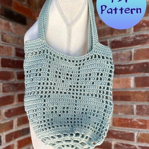 May include: A light blue crocheted tote bag with a wide, open top and a single handle. The bag is hanging on a white mannequin against a brick wall. The text "PDF Pattern" is in a blue circle in the upper right corner of the image.