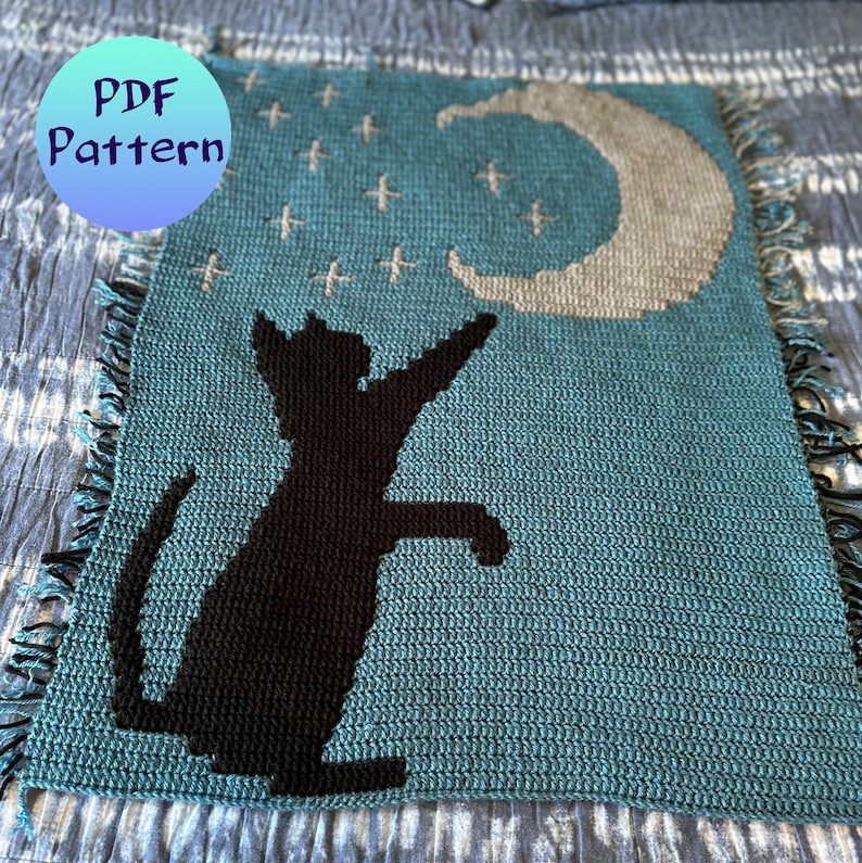 May include: A crochet pattern for a teal blue blanket featuring a black cat silhouette reaching up to a crescent moon. The pattern includes white stars.