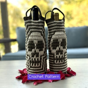 Puede incluir: Dos porta botellas de vino de ganchillo con un diseño de calavera en verde y blanco. Los porta botellas están sobre una mesa con pétalos de rosa roja.