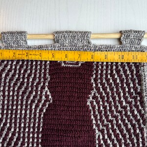 May include: A burgundy and gray crocheted wall hanging with a geometric pattern. The hanging is approximately 12 inches wide.