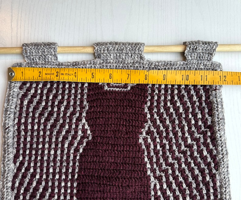 May include: A burgundy and gray crocheted wall hanging with a geometric pattern. The hanging is approximately 12 inches wide.