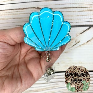 May include: A blue glitter seashell shaped badge holder with a clear retractable badge reel.