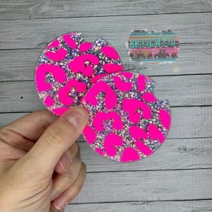 May include: Two round pink and silver glitter coasters with a leopard print design.
