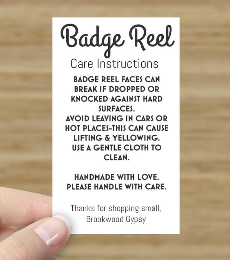 May include: A white rectangular card with the words "Badge Reel" in a cursive font. The card includes care instructions, such as avoiding extreme temperatures and handling with care. The text "Handmade with love" is also included.