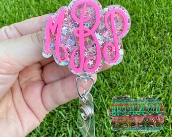 May include: Pink glitter resin badge holder with a clear retractable badge reel. The holder features a pink monogram with the letters "MBP".
