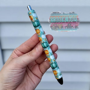 May include: A decorative pen with a teal background and a pattern of pumpkins in orange, teal, and white. The pen has a silver tip and a black tip. The text "BROOKWOOD" is visible in the background.
