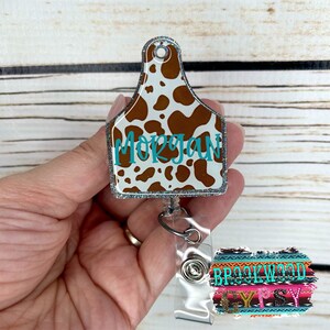 May include: Cow print badge holder with a retractable reel and a clear plastic badge holder. The badge holder has the name "Morgan" printed on it in turquoise blue lettering. The retractable reel has a colorful patterned fabric attached to it.