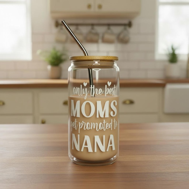 Puede incluir: Un vaso de vidrio transparente con tapa de bamb&uacute; y pajita de acero inoxidable. El vaso est&aacute; lleno de un l&iacute;quido marr&oacute;n claro y presenta el texto blanco "only the best MOMS get promoted to NANA".