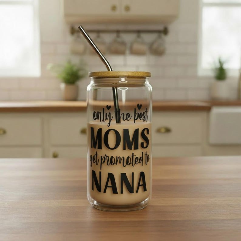 Puede incluir: Un vaso de vidrio transparente con tapa de bamb&uacute; y pajita de acero inoxidable. El vaso est&aacute; lleno de una bebida de color claro y presenta el texto "only the best MOMS get promoted to NANA" en letras negras.