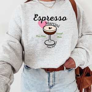 May include: Gray sweatshirt with a graphic of a coffee martini with the text "Espresso Martini" and "Social Club" in green text, "Tini Time" in green text, and "Extra Espresso" in green text.