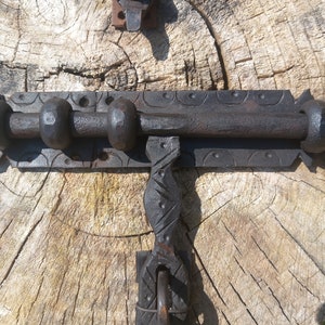 May include: A black metal door latch with intricate details, mounted on a weathered wooden surface.