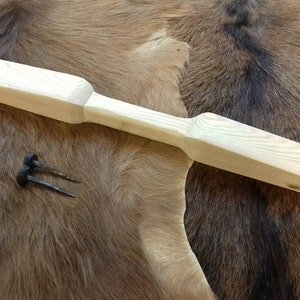 May include: A light-coloured wooden paddle with a handle and two metal nails. The paddle is approximately 46 cm long. The items are displayed on a brown, textured surface.