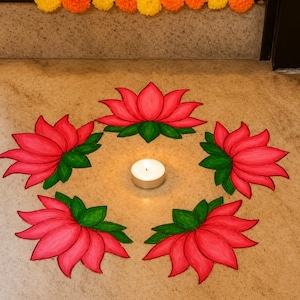 May include: A circular arrangement of five hand-drawn pink lotus flowers with green leaves on a light-colored floor. A single white tea light candle sits in the center of the floral pattern. A row of yellow and orange marigold flowers is visible.