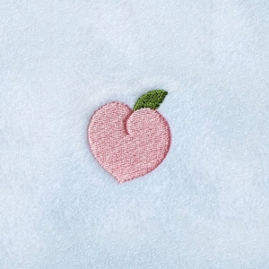May include: A pink peach with a green leaf embroidered on a white towel.