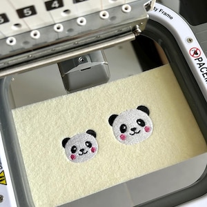 May include: Close-up of an embroidery machine stitching two panda bear designs onto a light yellow fabric. Each panda has black ears, eyes, and a nose, with pink cheeks. The machine's frame and numbered components are visible.