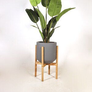 May include: A gray ceramic planter with a wooden stand, featuring a green artificial bird of paradise plant.
