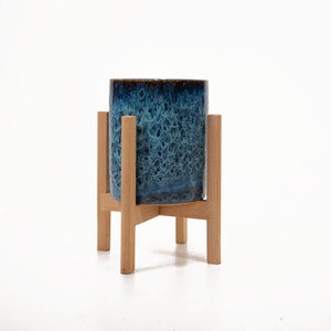 May include: A blue ceramic planter with a brown glaze sits on a wooden stand with four legs.