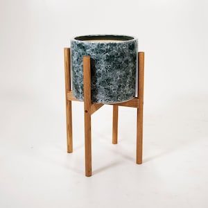 May include: A green and white ceramic planter with a wood stand. The planter has a mottled pattern and the stand has a simple design.
