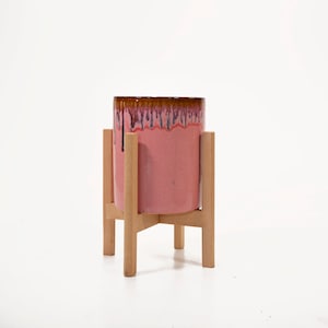 May include: A pink ceramic planter with a brown glaze sits on a wooden stand with four legs.