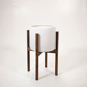 May include: White ceramic planter on a wooden stand. The stand has four legs and a crossbar.
