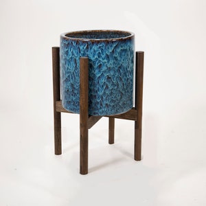 May include: A blue and brown ceramic planter on a wooden stand. The planter has a textured, wavy design.