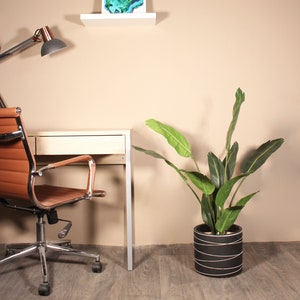 May include: A brown leather office chair with a chrome base sits next to a light wood desk with a white shelf above it. A green plant in a black and white striped pot is on the right side of the image.