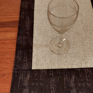 May include: A black and gray placemat with a textured design. A clear glass wine glass sits on top of the placemat.