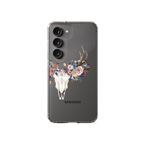 以下が含まれることがあります： 背面に「SAMSUNG」の文字が印刷された、花柄の頭蓋骨のデザインが施された透明な携帯電話ケースです。