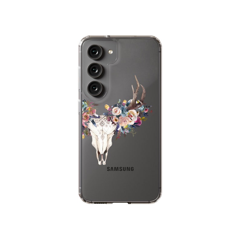 以下が含まれることがあります： 背面に「SAMSUNG」の文字が印刷された、花柄の頭蓋骨のデザインが施された透明な携帯電話ケースです。