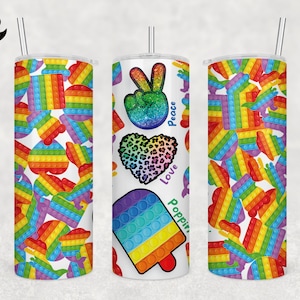 May include: Three white tumblers with different designs. The first tumbler has a rainbow pop-it pattern. The second tumbler has a rainbow pop-it popsicle, a heart with a leopard print, a peace sign with glitter, and the words "Peace, Love, Poppin". The third tumbler has a rainbow pop-it pattern.