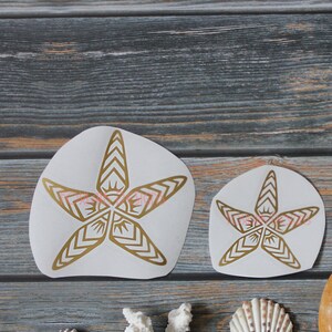 May include: A collection of seashells, including sand dollars, starfish, and a coral piece. The starfish are decorated with a gold and pink geometric design.
