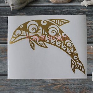 May include: A gold tribal dolphin silhouette decal on a white background. The dolphin is leaping out of the water with its tail in the air. The decal is perfect for adding a touch of ocean charm to any surface.