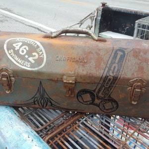 May include: A rusty metal toolbox with a black and white wrench graphic and the text "TOOL". The toolbox has a sticker that says "Arizona Bay Swimmers 46.2".