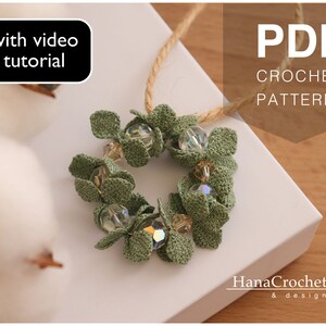May include: A green crocheted wreath with clear glass beads, on a white surface. The text "PDF CROCHET PATTERN" is in the upper right corner of the image. The text "with video tutorial" is in the upper left corner of the image.